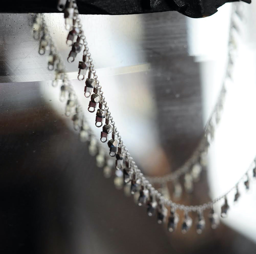 A sterling silver fringe-style necklace hangs off of a vintage mirror and catches light.